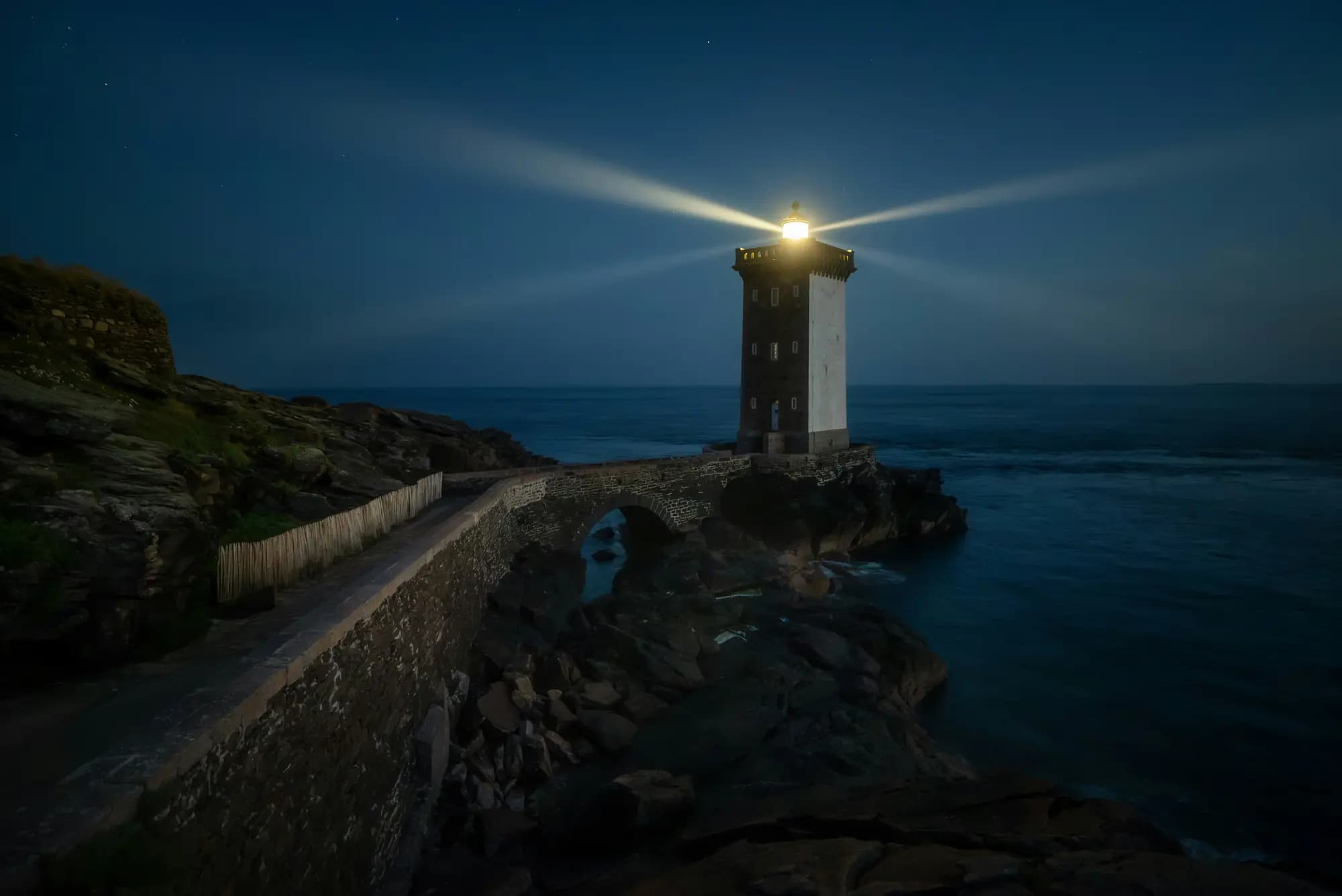A lighthouse beam cutting across a night sky over the sea