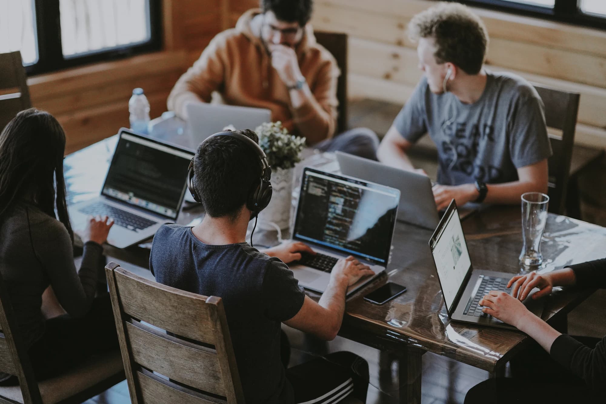 Small team working on laptops around a shared wooden table in a warm, timber-lined studio