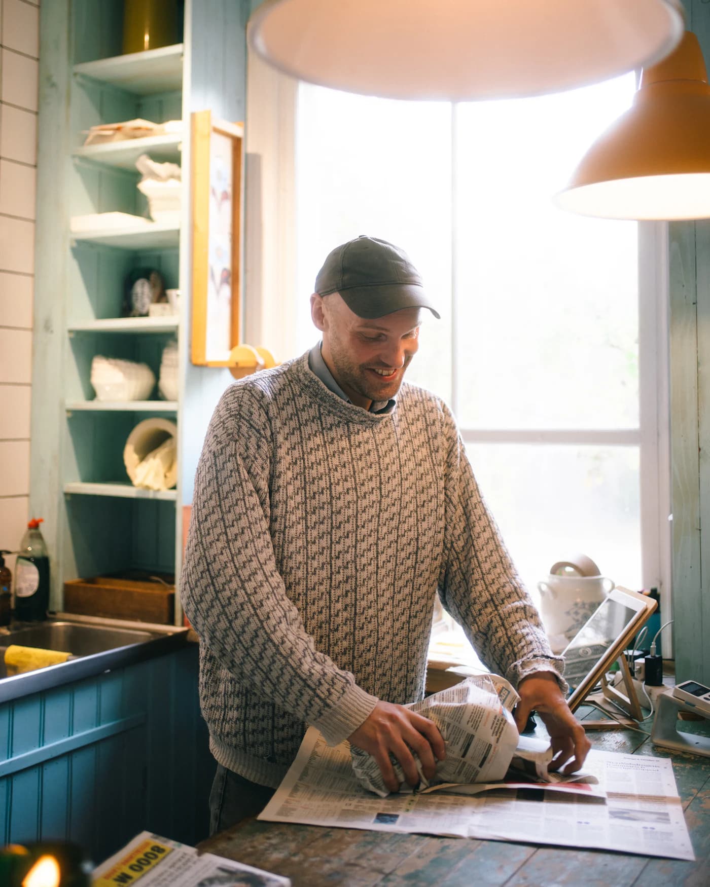 Smiling shop owner wrapping an item in newspaper at the counter of a small timber-and-teal store